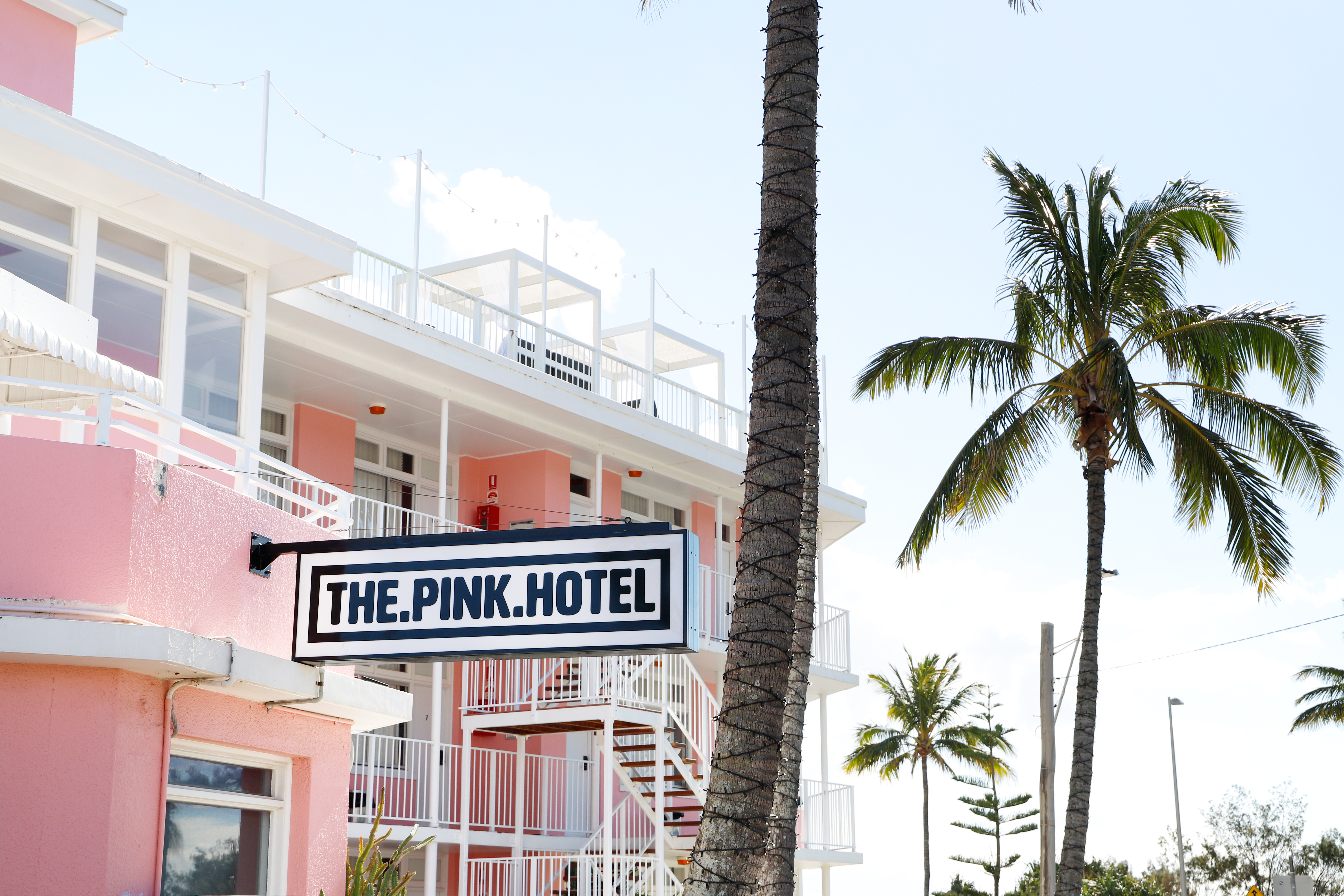 Bright pink exterior of retro hotel The Pink Hotel, surrounded by palm trees 